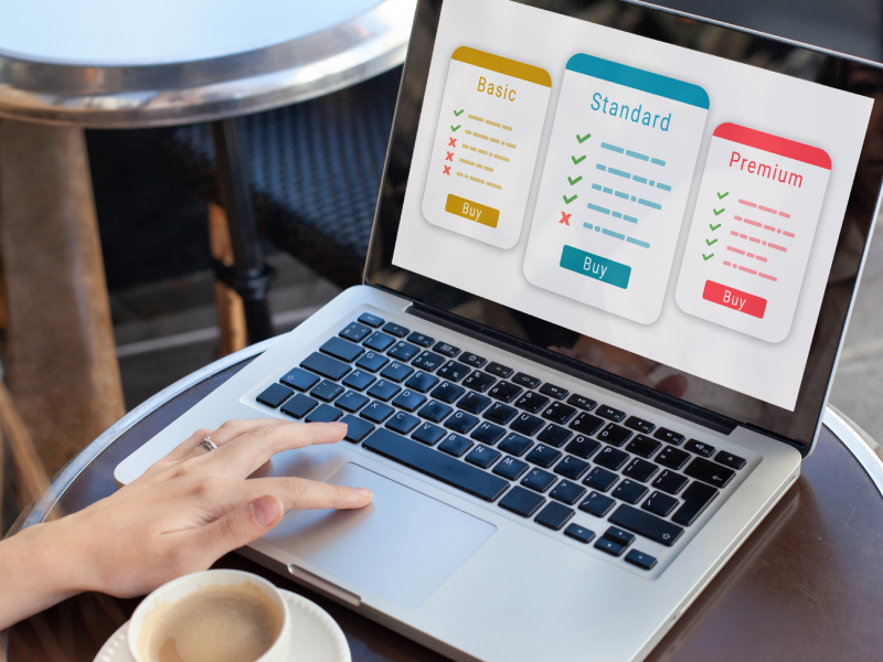 Laptop displaying pricing plans, hand on keyboard.