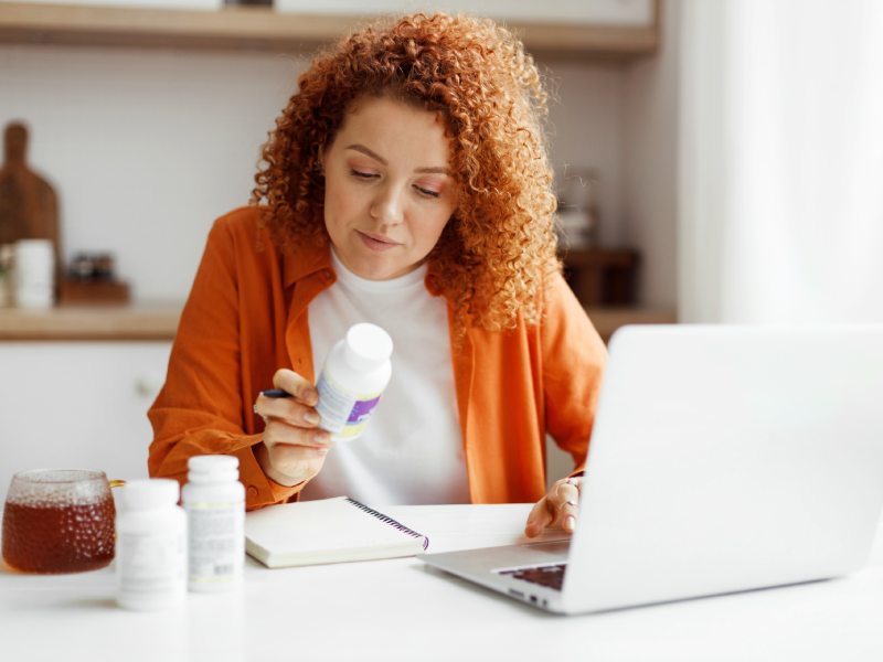 Woman examining supplement bottle at desk.